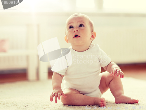 Image of happy baby boy or girl sitting on floor at home