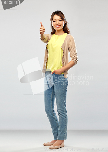 Image of happy asian woman showing thumbs up over grey