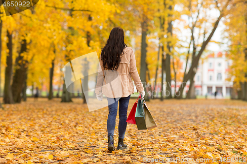 Image of woman with shopping bags walking along autumn park