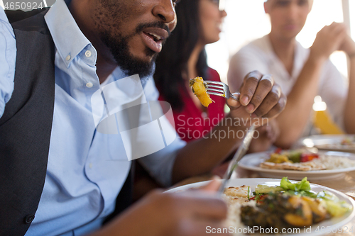 Image of african man eating with friends at restaurant