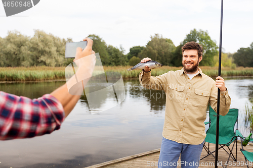 Image of friend photographing fisherman with fish at lake