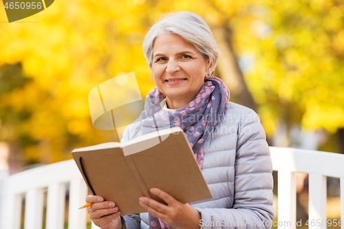 Image of happy senior woman reading diary at autumn park
