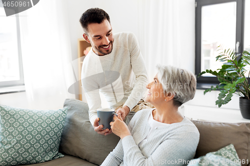 Image of adult son bringing coffee to senior mother at home