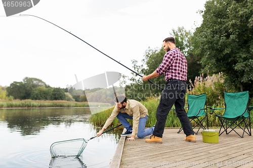 Image of male friends with net and fishing rods on lake