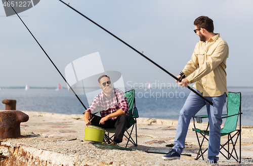 Image of male friends with fishing rods on sea pier