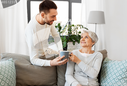 Image of adult son bringing coffee to senior mother at home