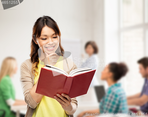 Image of happy asian woman reading book at school