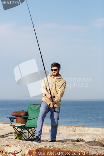 Image of bearded fisherman with fishing rod on sea pier
