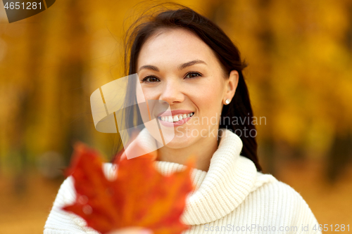 Image of happy young woman with maple leaf in autumn park