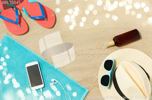 Image of smartphone, hat, flip flops and shades on beach