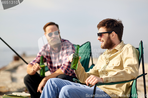 Image of happy friends fishing and drinking beer on pier