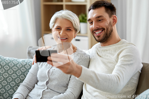 Image of senior mother with adult son taking selfie at home