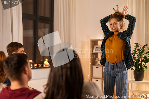 Image of happy friends playing charades at home in evening