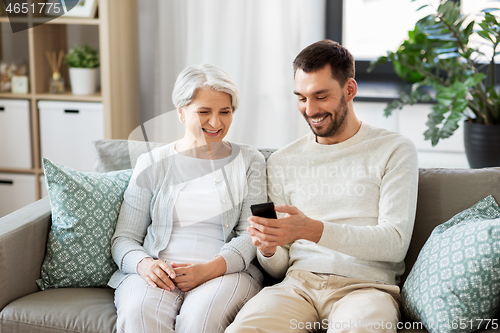 Image of old mother and adult son with smartphone at home