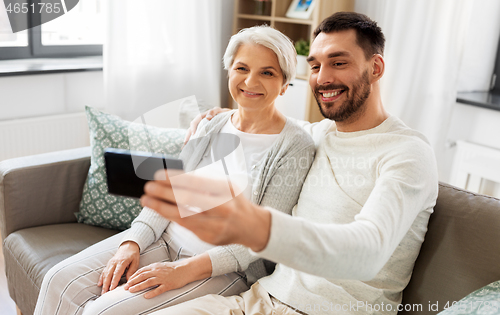 Image of senior mother with adult son taking selfie at home