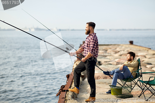 Image of happy friends with fishing rods on pier