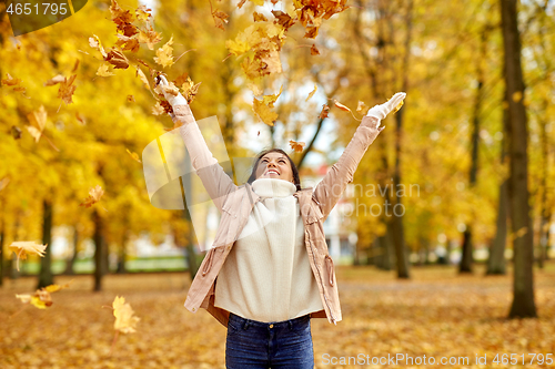 Image of happy woman having fun with leaves in autumn park