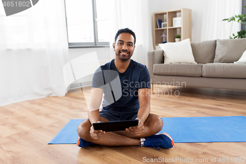 Image of indian man with tablet pc and exercise mat at home