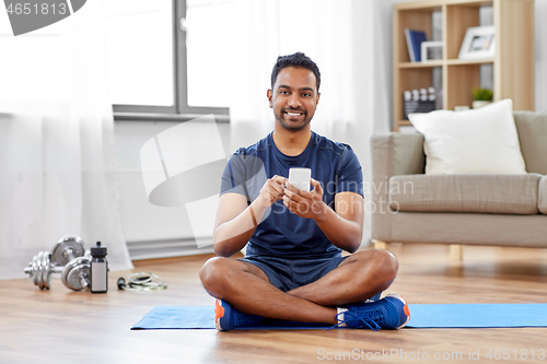 Image of indian man with smartphone on exercise mat at home