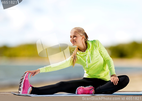 Image of woman stretching on exercise mat on beach