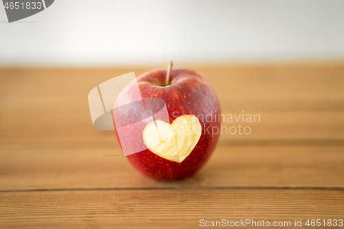 Image of red apple with carved heart shape on wooden table