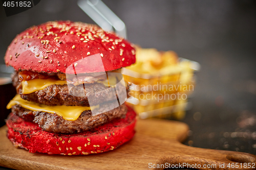 Image of Homemade red sesame bun double bacon cheese burger. Served with french fries on wooden board.