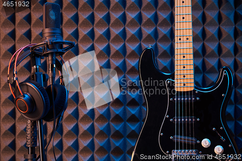 Image of Black electric guitar and microphone with professional headphones