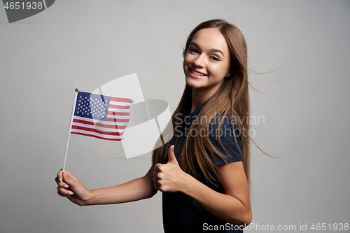 Image of Happy female holding USA flag and gesturing thumb up