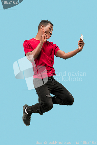 Image of always on mobile. Full length of handsome young man taking phone while jumping