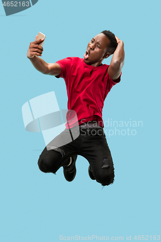 Image of always on mobile. Full length of handsome young man taking phone while jumping