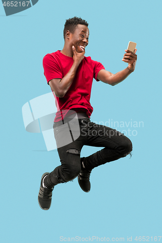 Image of always on mobile. Full length of handsome young man taking phone while jumping