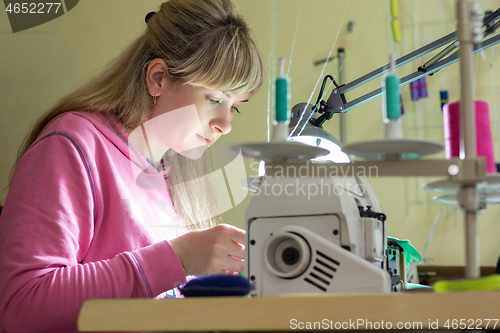 Image of Girl happily sews on a professional sewing machine