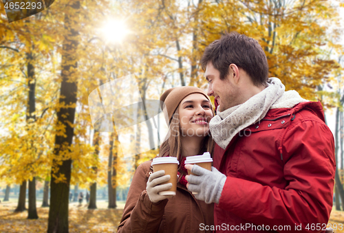 Image of happy couple with coffee walking in autumn park