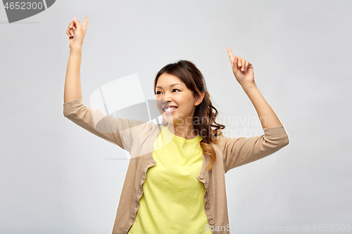 Image of happy asian woman dancing over grey background