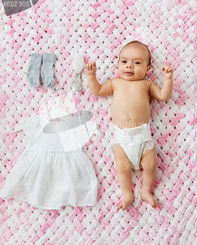 Image of baby girl in diaper lying with dress on blanket