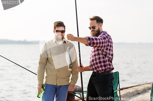 Image of male friends with fishing rods and beer on pier