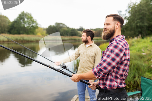 Image of male friends with fishing rods on lake pier