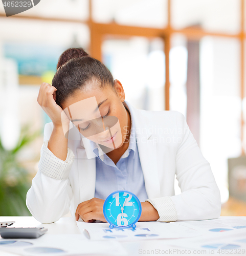 Image of tired businesswoman with alarm clock at office