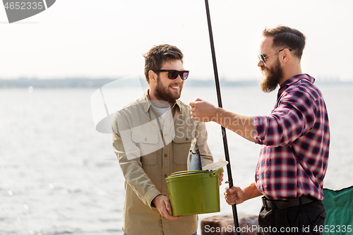 Image of male friends with fish and fishing rods on pier