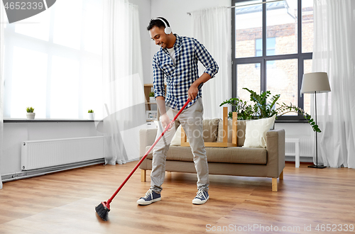 Image of man in headphones with broom cleaning at home