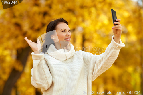 Image of woman taking selfie by smartphone at autumn park