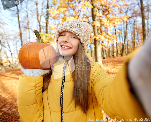 Image of girl with pumpkin taking selfie at autumn park