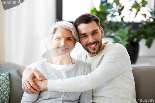 Image of senior mother with adult son hugging at home