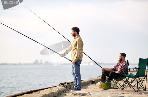 Image of happy friends with fishing rods on pier