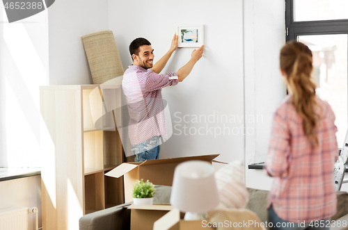 Image of happy couple moving to new home and hanging photo