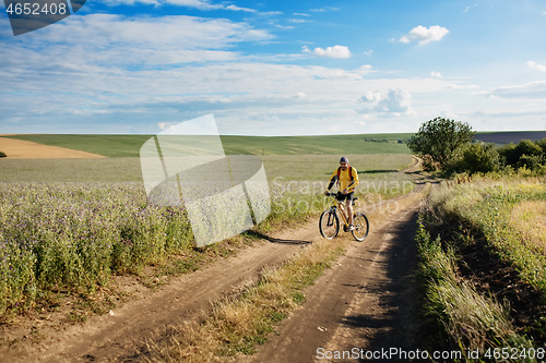 Image of Cyclist riding a bike on off road to the sunset