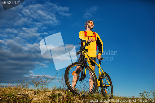 Image of Cyclist man standing on top of a mountain with bicycle