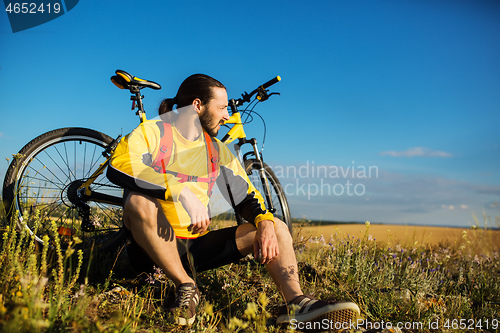 Image of Cyclist resting on grass in mountains. Man is looking aside.