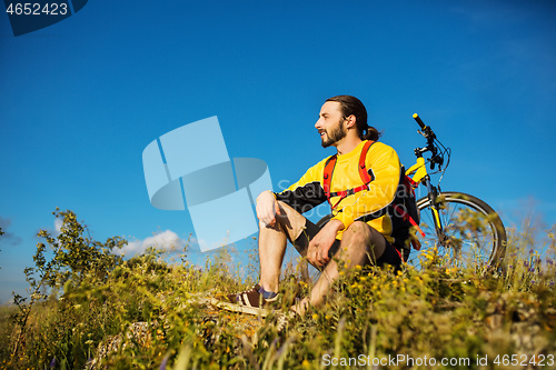 Image of Cyclist resting on grass in mountains. Man is looking aside.