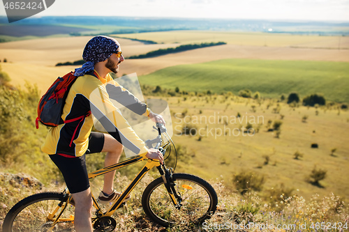 Image of Cyclist riding a bike on off road to the sunset